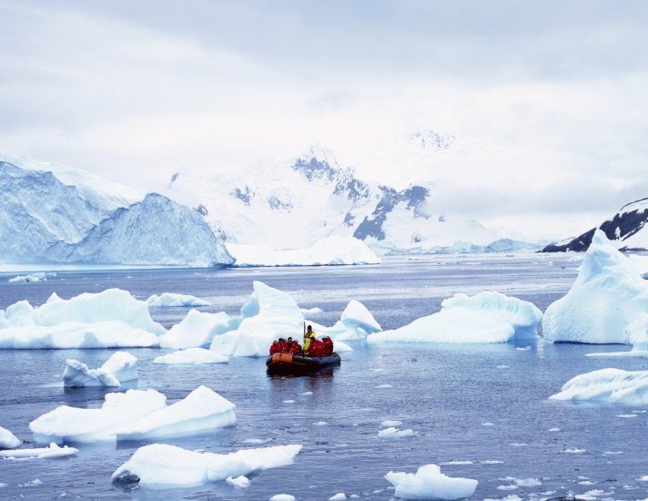 Panoramic view of ecological tourists in inflatable Zodiac boat with glaciers and icebergs in Paradise Harbor, Antarctica